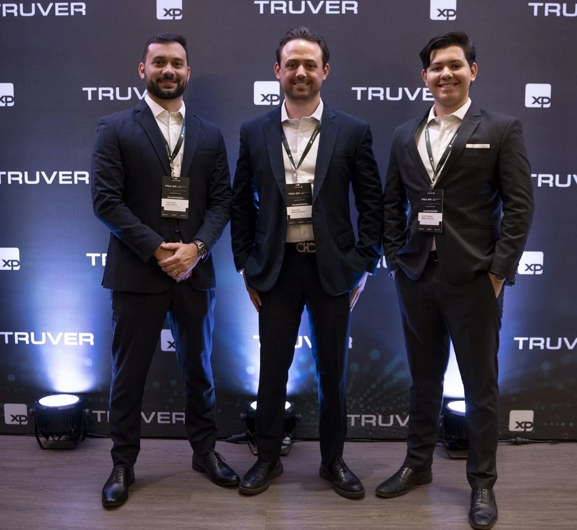 Anfitriões do Truver Experience 2024 diante do painel Truver e XP.
